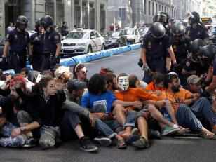 Un grupo de indignados sentados en el suelo, tras ellos policías