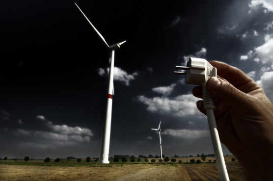 foto simbólica, un aerogenerador y una mano con un enchufe eléctrico