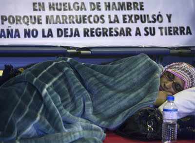 Aminetou tumbada en el suelo del aeropuerto con una pancarta detrás