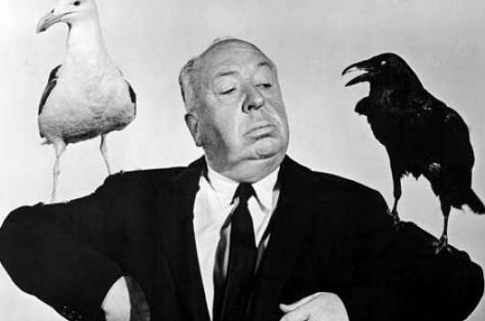 Alfred Hitchcock con un pájaro blanco y otro negro en los hombros