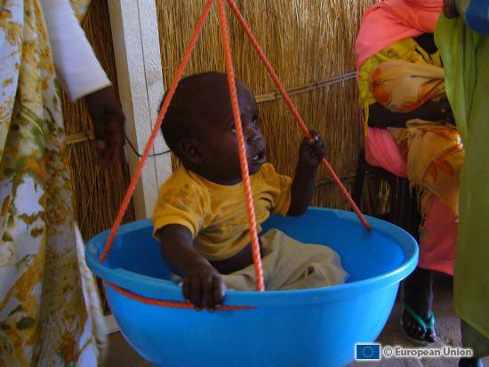 En un campo de refugiados pesan a un bebé sentado en una palangana