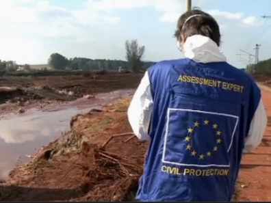 Una persona con un chaleco de protección civil de la UE ante un terreno inundado 