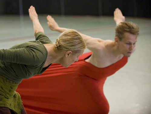 Carolyn Carlson marca un paso al bailarín que lleva un ropaje de color naranja