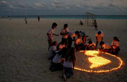 Representantes de una ONG encienden velas en la playa haciendo la forma del mundo