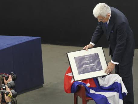 El presidente del Parlamento pone el diploma sobre una silla en la que hay una bandera cubana