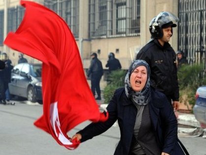 Una mujer ondea una bandera de Túnez, detrás un policía