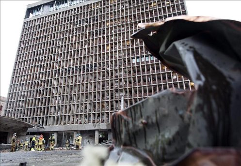 Fachada del edificio muy dañada, en primer plano lo que parecen los restos de un vehículo